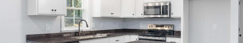Custom home features in a Central Virginia home: white kitchen cabinets, stainless steel appliances, and dark marble countertop with a window view.
