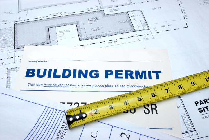 An example of a building permit required in Virginia, laid out on a table over architectural blueprints, with a tape measure resting atop it.