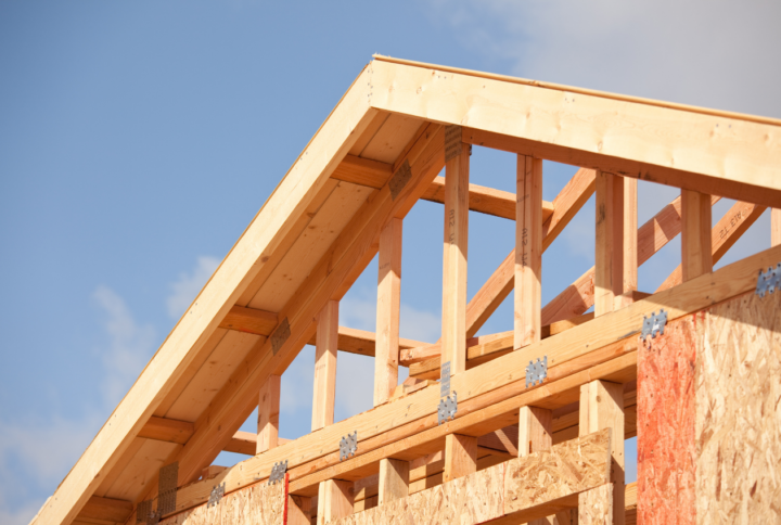 Wooden roof rafters and trusses under a blue sky.