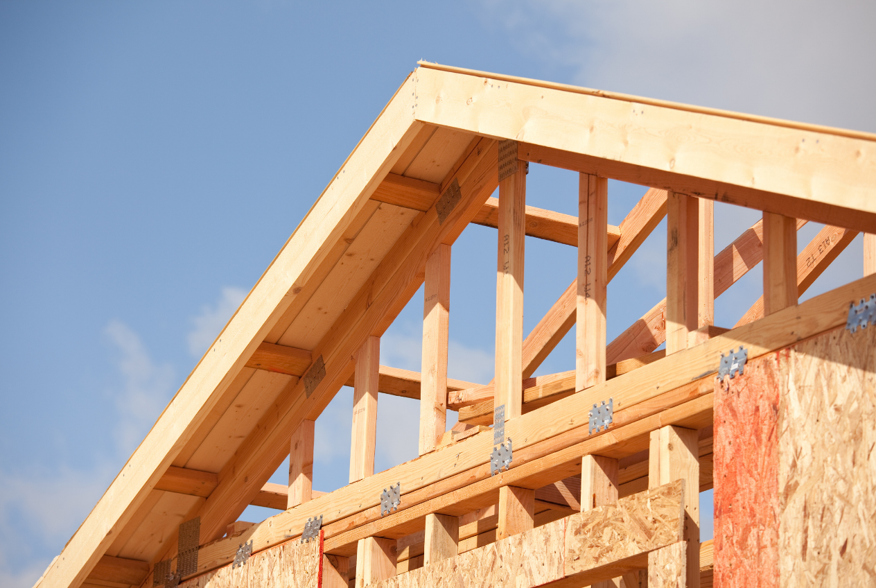 Wooden roof rafters and framing against a blue sky.